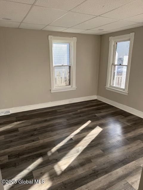 empty room with a paneled ceiling, dark hardwood / wood-style floors, and a healthy amount of sunlight