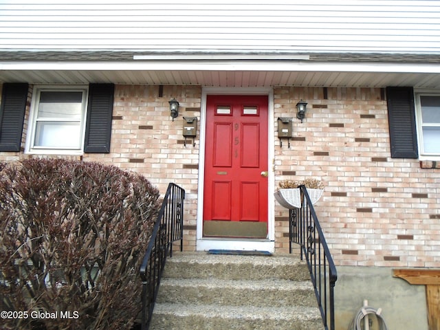 doorway to property with brick siding and a shingled roof