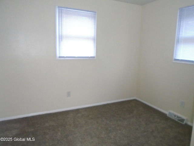 spare room with plenty of natural light, baseboards, visible vents, and dark carpet