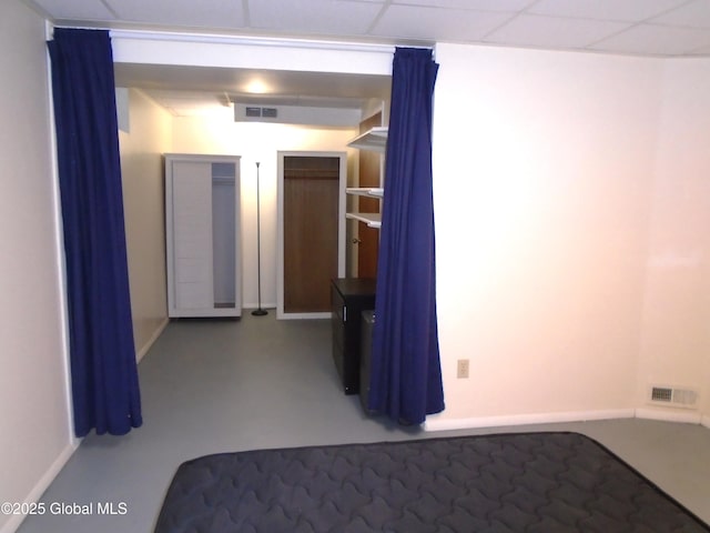 empty room with a drop ceiling, baseboards, visible vents, and finished concrete floors