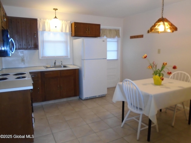 kitchen featuring freestanding refrigerator, a sink, hanging light fixtures, light countertops, and stainless steel microwave