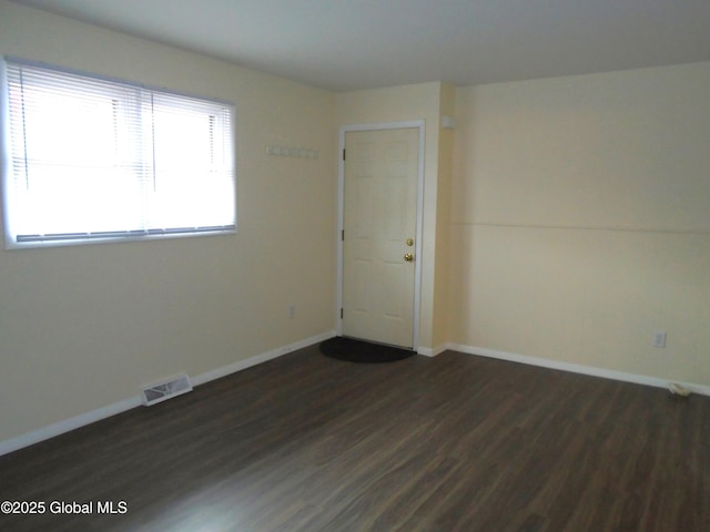 spare room featuring visible vents, baseboards, and dark wood-style flooring