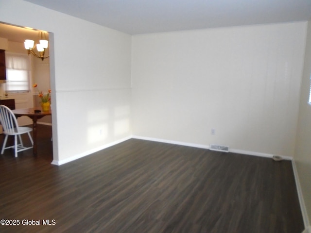 spare room with dark wood finished floors, a notable chandelier, visible vents, and baseboards