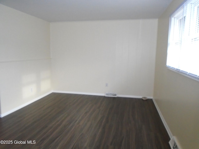 unfurnished room featuring visible vents, baseboards, and dark wood finished floors