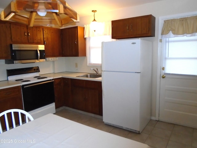 kitchen featuring electric stove, a sink, stainless steel microwave, freestanding refrigerator, and light countertops