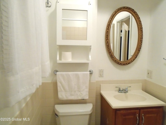 full bathroom featuring a wainscoted wall, toilet, shower / tub combo with curtain, tile walls, and vanity