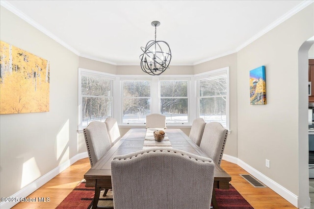 dining area with an inviting chandelier, a wealth of natural light, ornamental molding, and light wood-type flooring