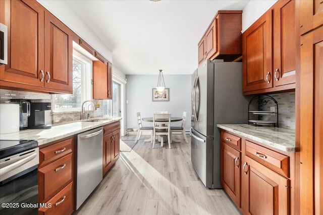 kitchen featuring pendant lighting, sink, stainless steel appliances, light stone countertops, and light wood-type flooring