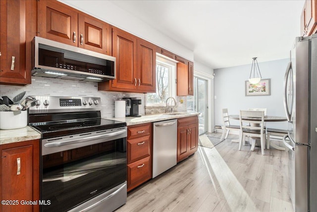 kitchen featuring appliances with stainless steel finishes, backsplash, light stone countertops, light hardwood / wood-style floors, and decorative light fixtures