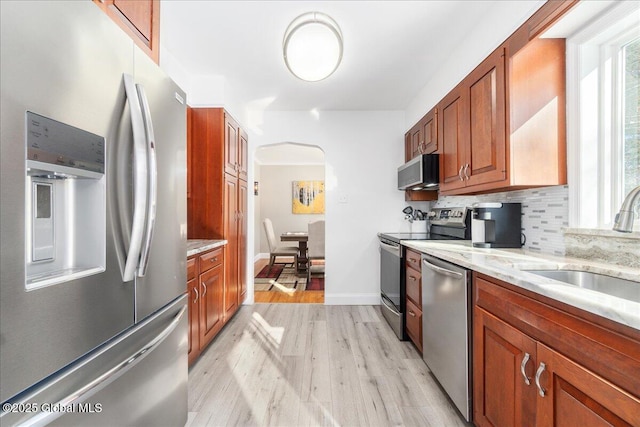 kitchen with appliances with stainless steel finishes, sink, decorative backsplash, light stone counters, and light hardwood / wood-style floors