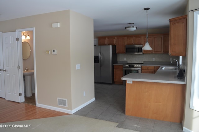 kitchen with pendant lighting, sink, appliances with stainless steel finishes, tasteful backsplash, and kitchen peninsula