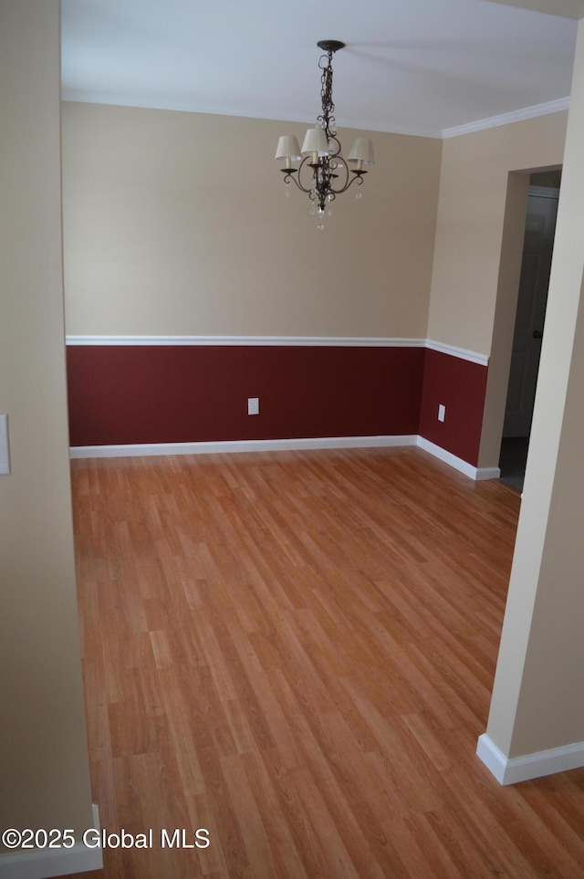 empty room with a notable chandelier, ornamental molding, and light wood-type flooring