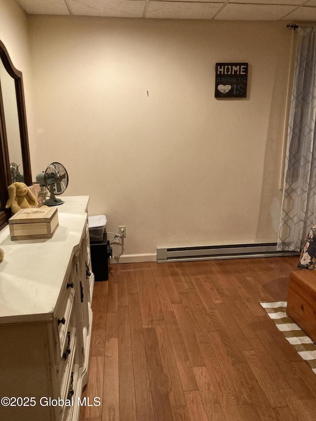 interior space with a baseboard radiator, a paneled ceiling, vanity, and wood finished floors