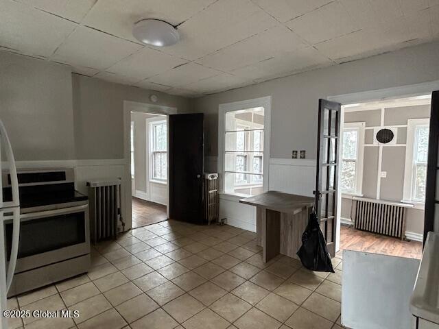 kitchen with stainless steel range with electric stovetop, light tile patterned floors, and radiator heating unit