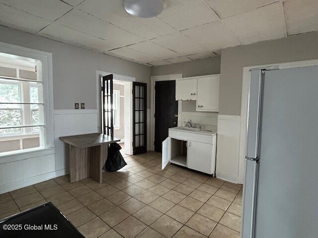 kitchen featuring white cabinetry, sink, light tile patterned flooring, and stainless steel fridge