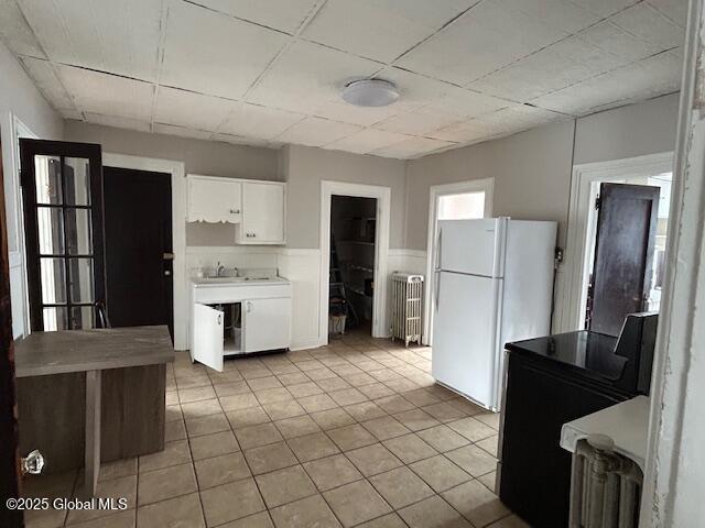 kitchen featuring radiator heating unit, sink, white cabinets, white refrigerator, and light tile patterned floors