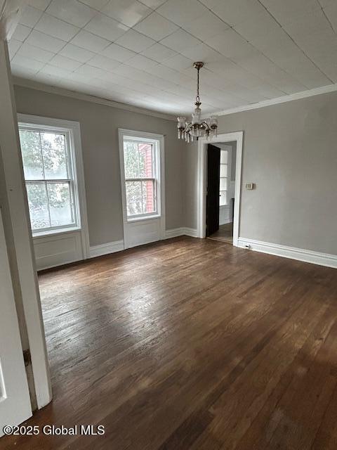 unfurnished dining area featuring dark hardwood / wood-style flooring, crown molding, and an inviting chandelier