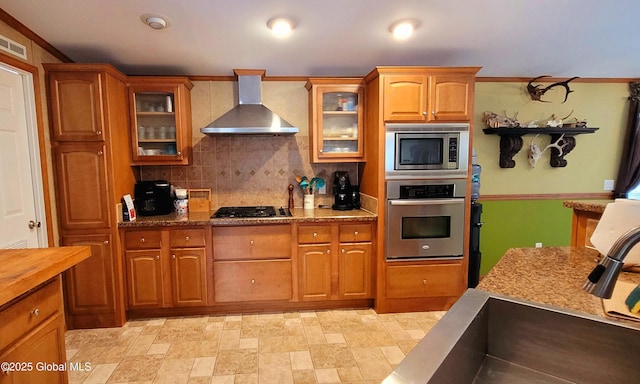 kitchen with tasteful backsplash, wall chimney exhaust hood, stainless steel appliances, and light stone counters