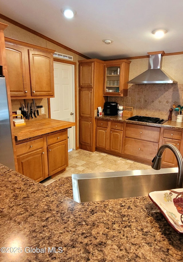 kitchen featuring black gas stovetop, stainless steel refrigerator, crown molding, and wall chimney exhaust hood