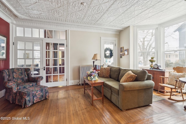 living room featuring wood-type flooring, ornamental molding, radiator heating unit, and french doors