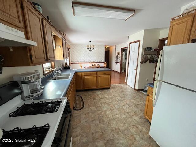 kitchen featuring sink, an inviting chandelier, hanging light fixtures, white refrigerator, and gas range oven