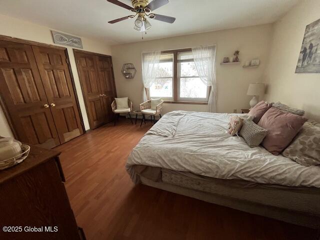 bedroom with ceiling fan, two closets, and dark hardwood / wood-style flooring