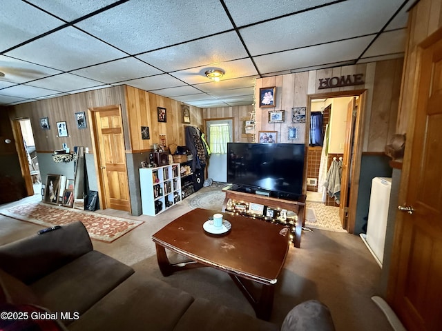 carpeted living room with wooden walls and a drop ceiling