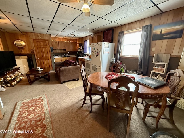 carpeted dining area with washer / clothes dryer, a paneled ceiling, and wood walls