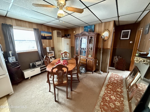 carpeted dining space with wooden walls, ceiling fan, and a paneled ceiling