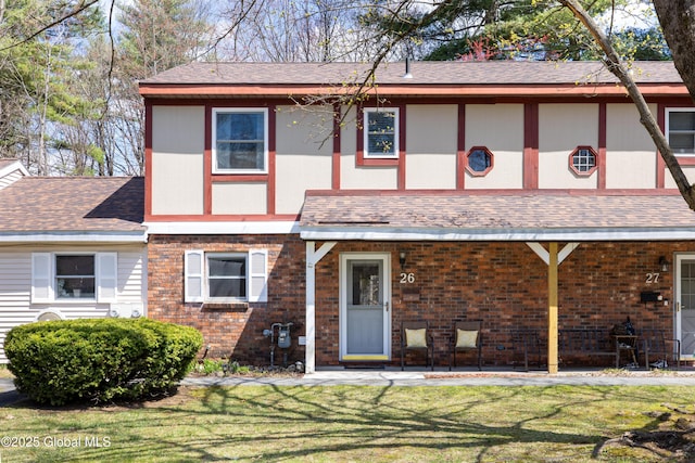 view of front of house with roof with shingles, brick siding, and a front lawn