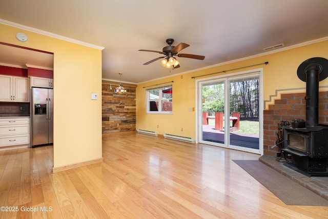 unfurnished living room with a baseboard radiator, ceiling fan, light wood-style flooring, and a wood stove