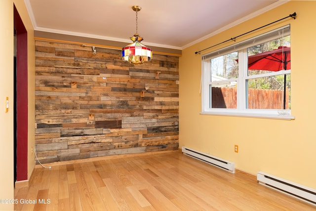 spare room featuring a baseboard heating unit, crown molding, wood walls, and wood finished floors
