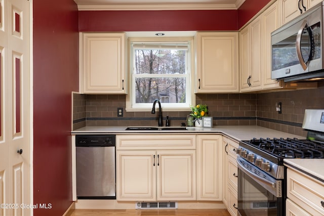kitchen featuring ornamental molding, cream cabinetry, a sink, and stainless steel appliances