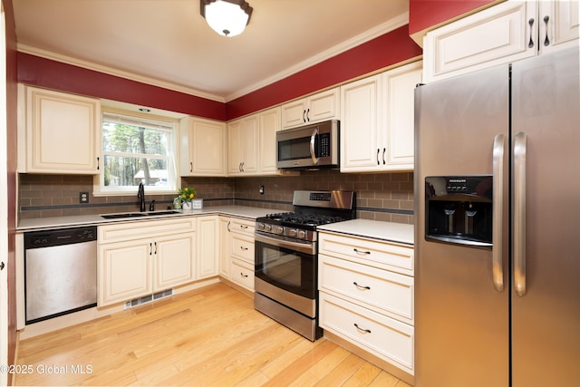 kitchen featuring appliances with stainless steel finishes, ornamental molding, light wood finished floors, a sink, and visible vents