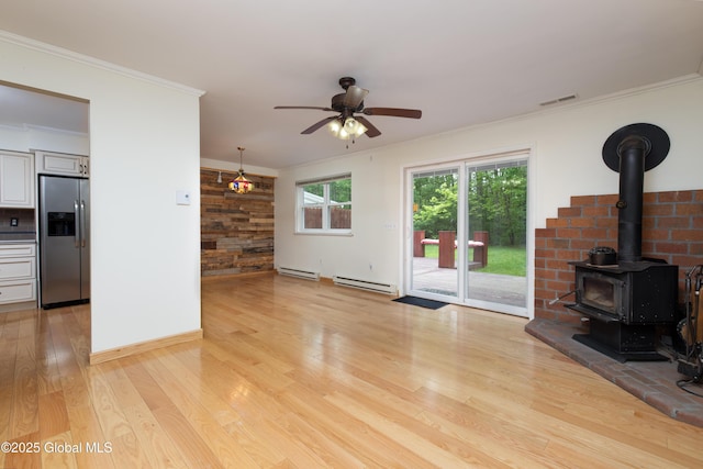 26 Queens Way, Queensbury, NY 12804 - unfurnished living room featuring a wood stove, a baseboard radiator, light wood finished floors, a ceiling fan, and ornamental molding