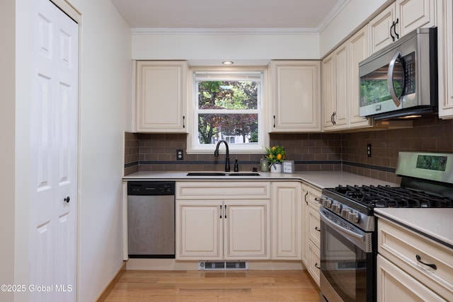 26 Queens Way, Queensbury, NY 12804 - kitchen with appliances with stainless steel finishes, a sink, crown molding, tasteful backsplash, and light wood-style floors
