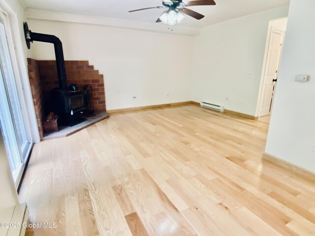 26 Queens Way, Queensbury, NY 12804 - unfurnished living room featuring a baseboard heating unit, a wood stove, wood finished floors, ceiling fan, and baseboards