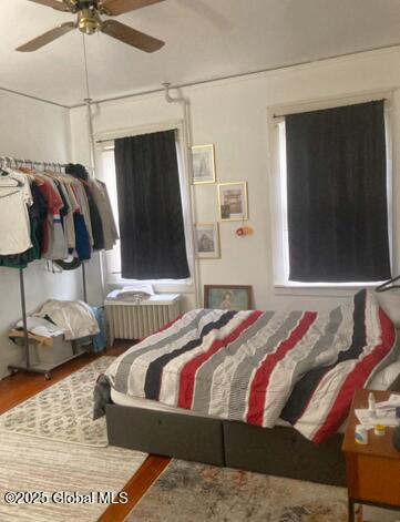 bedroom featuring wood-type flooring, radiator heating unit, and ceiling fan