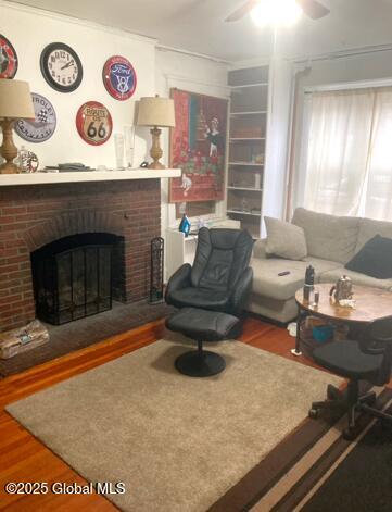 living room with a brick fireplace, hardwood / wood-style floors, and ceiling fan