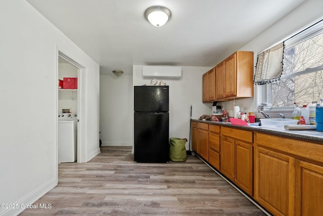 kitchen with a wall mounted air conditioner, washer / dryer, light wood-type flooring, and black fridge