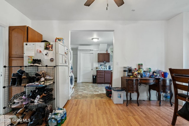 kitchen featuring a wall mounted AC, stacked washer and dryer, white fridge, ceiling fan, and light hardwood / wood-style flooring