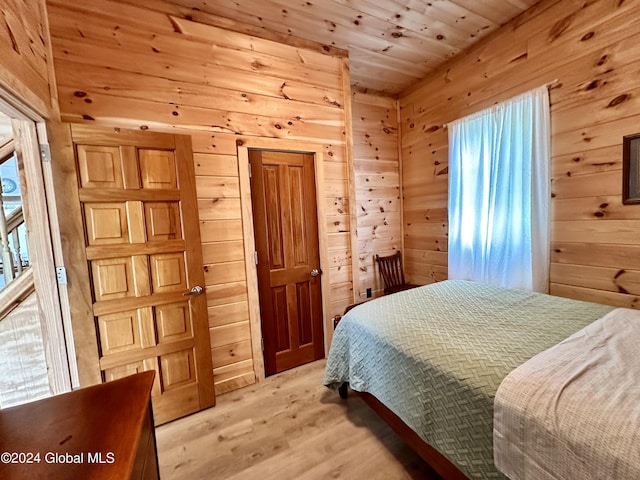 bedroom featuring multiple windows, light hardwood / wood-style floors, and wood walls