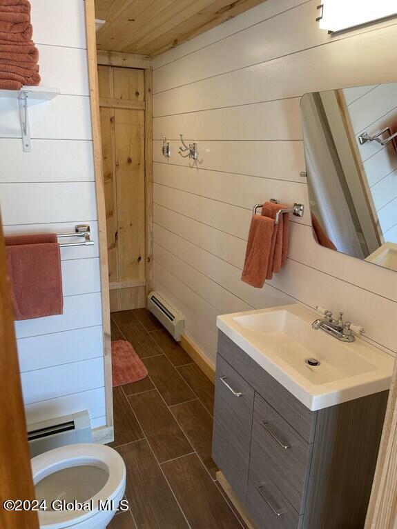 bathroom with vanity, a baseboard heating unit, and wood walls