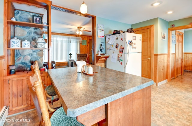 kitchen with white refrigerator, ceiling fan, a baseboard heating unit, and wooden walls