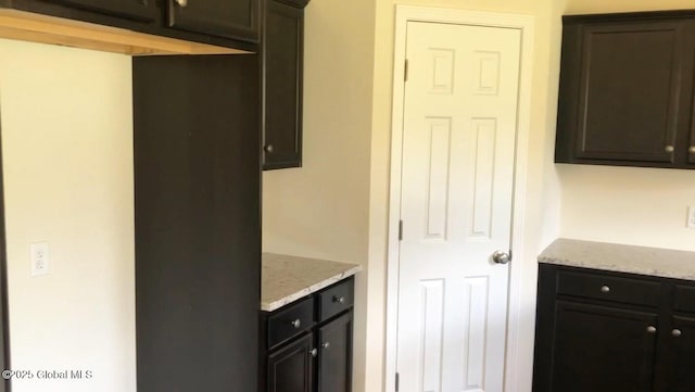 kitchen featuring light stone counters and dark brown cabinets