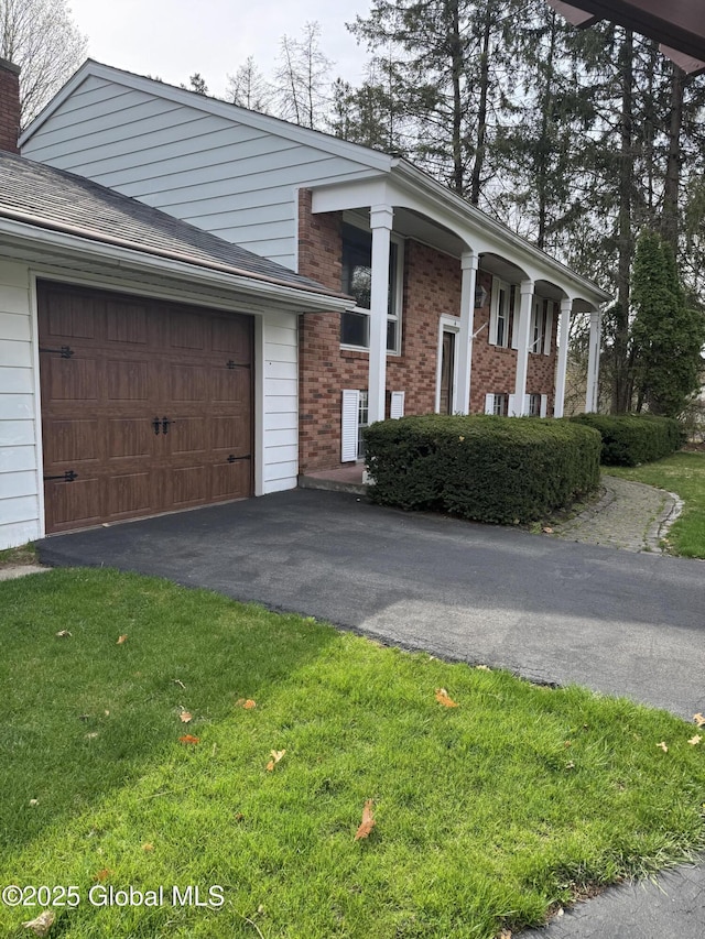 view of side of home with a chimney, a yard, brick siding, driveway, and an attached garage