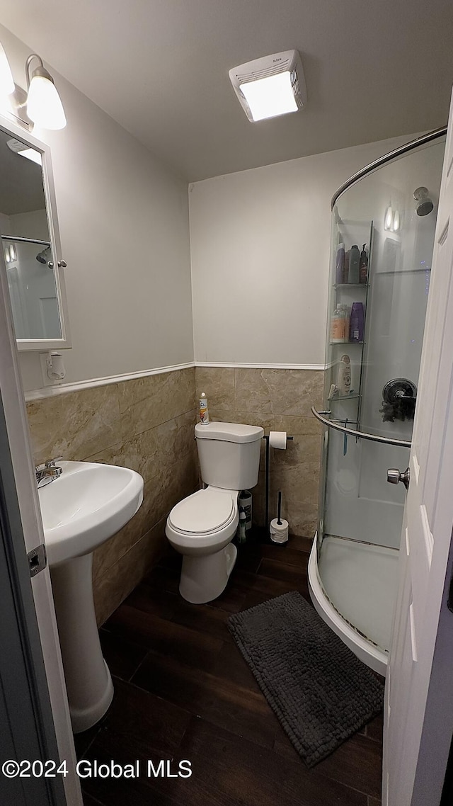 bathroom with tile walls, hardwood / wood-style flooring, toilet, and a shower