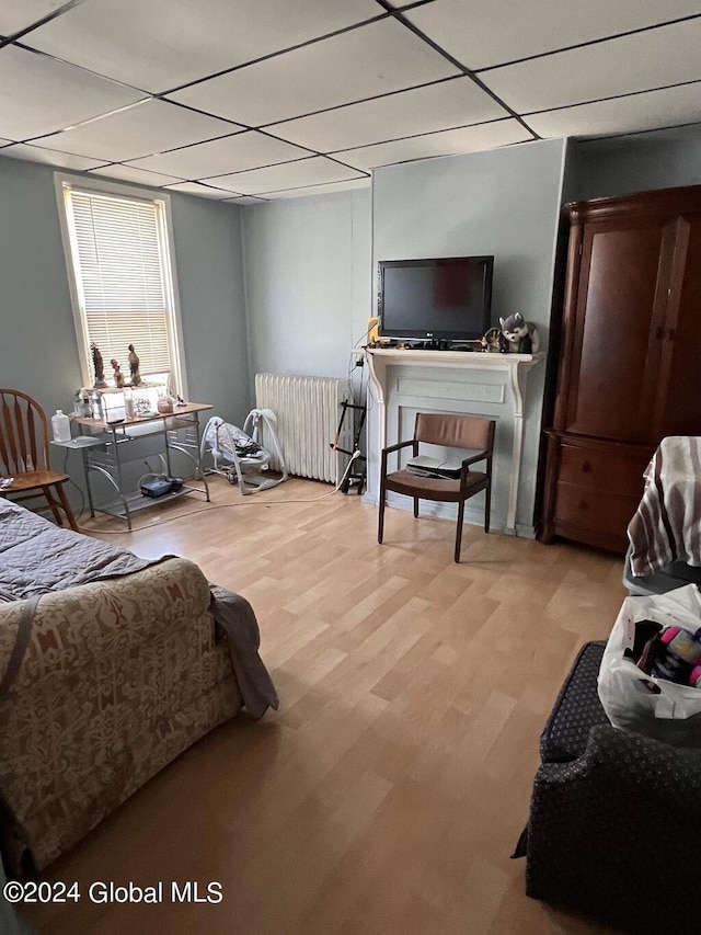 bedroom with a paneled ceiling, radiator heating unit, and light hardwood / wood-style floors