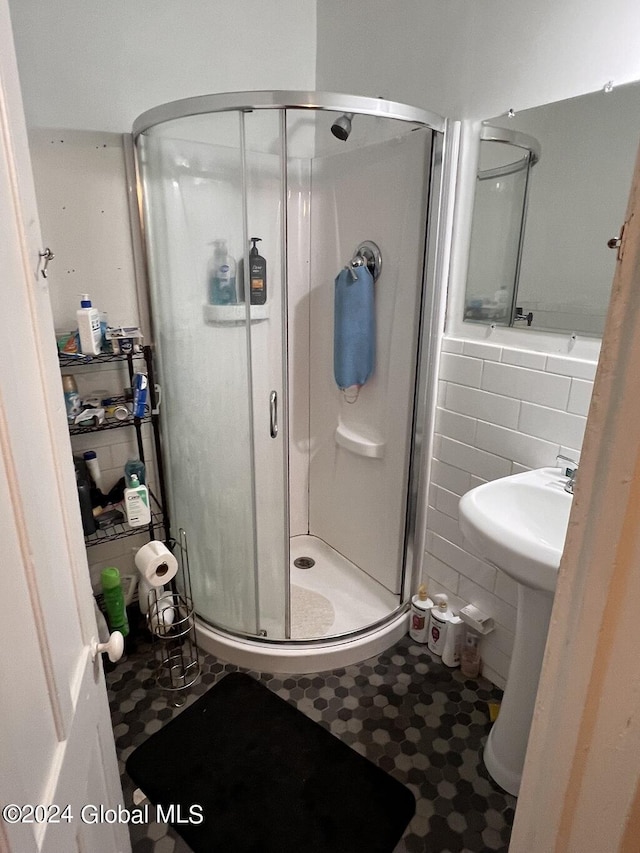 bathroom featuring a shower with door, sink, and tile walls