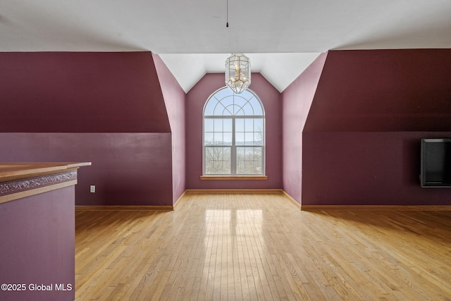 additional living space with vaulted ceiling, a chandelier, and light wood-type flooring